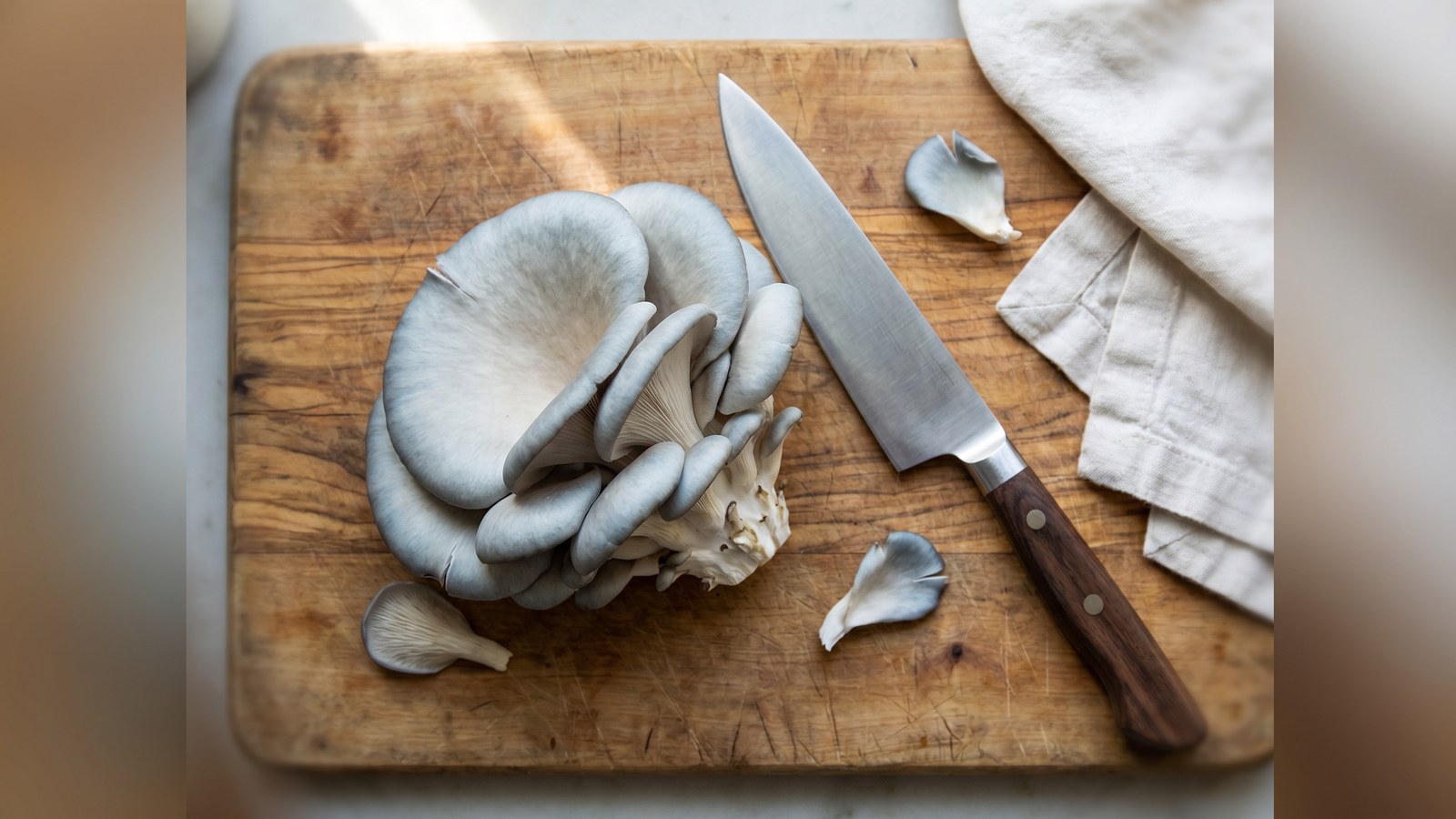 Fresh blue oyster mushroom cluster on a wood cutting board with chef's knife