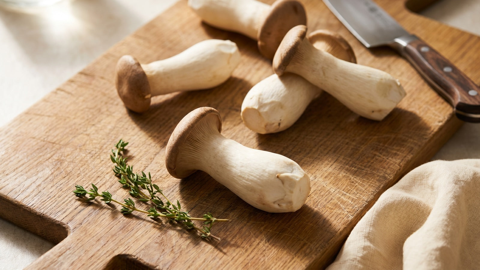 Whole king trumpet mushrooms with thick white stems and small brown caps arranged on a wooden cutting board in soft natural light