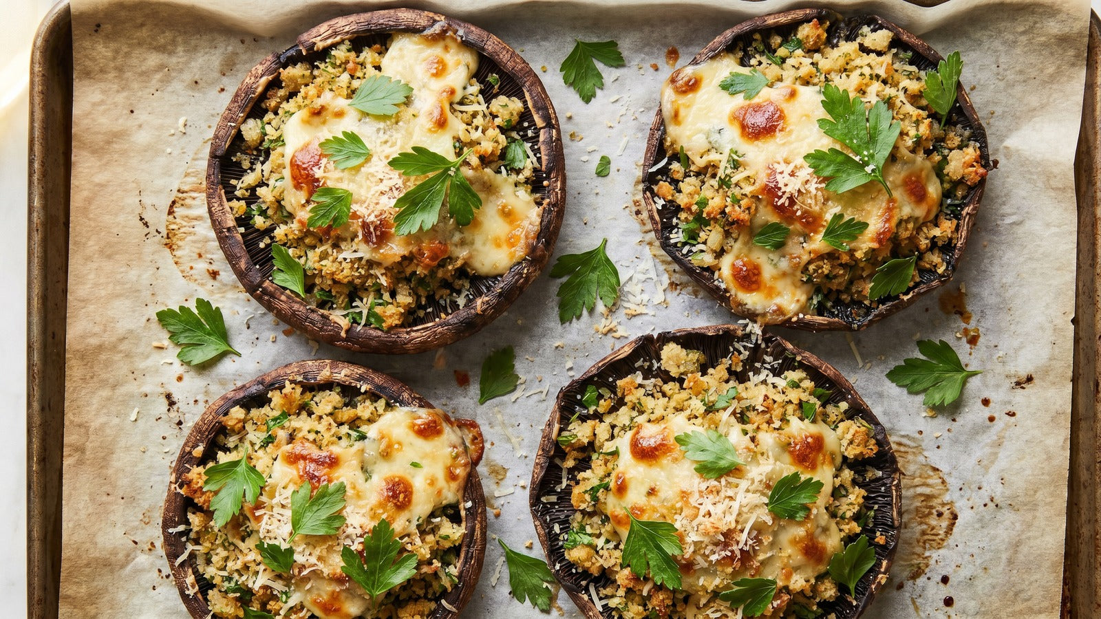 Large portobello mushroom caps stuffed with golden herbed breadcrumb filling on a baking sheet